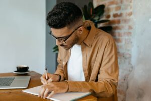 a-man-wearing-a-brown-long-sleeve-shirt-writing-on-notebook